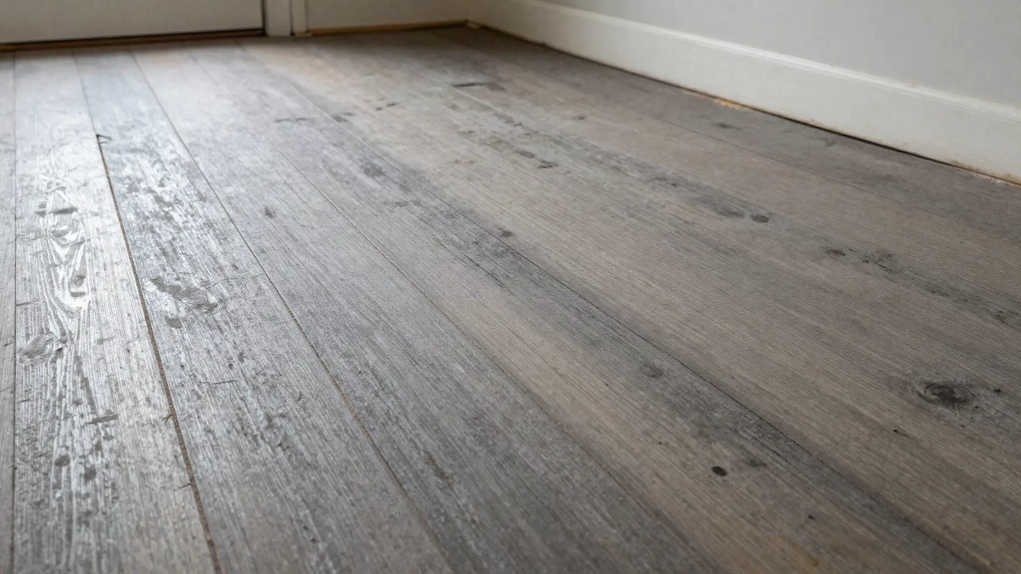 Worn hardwood floor with the finish scuffed through to bare grey wood along a traffic path