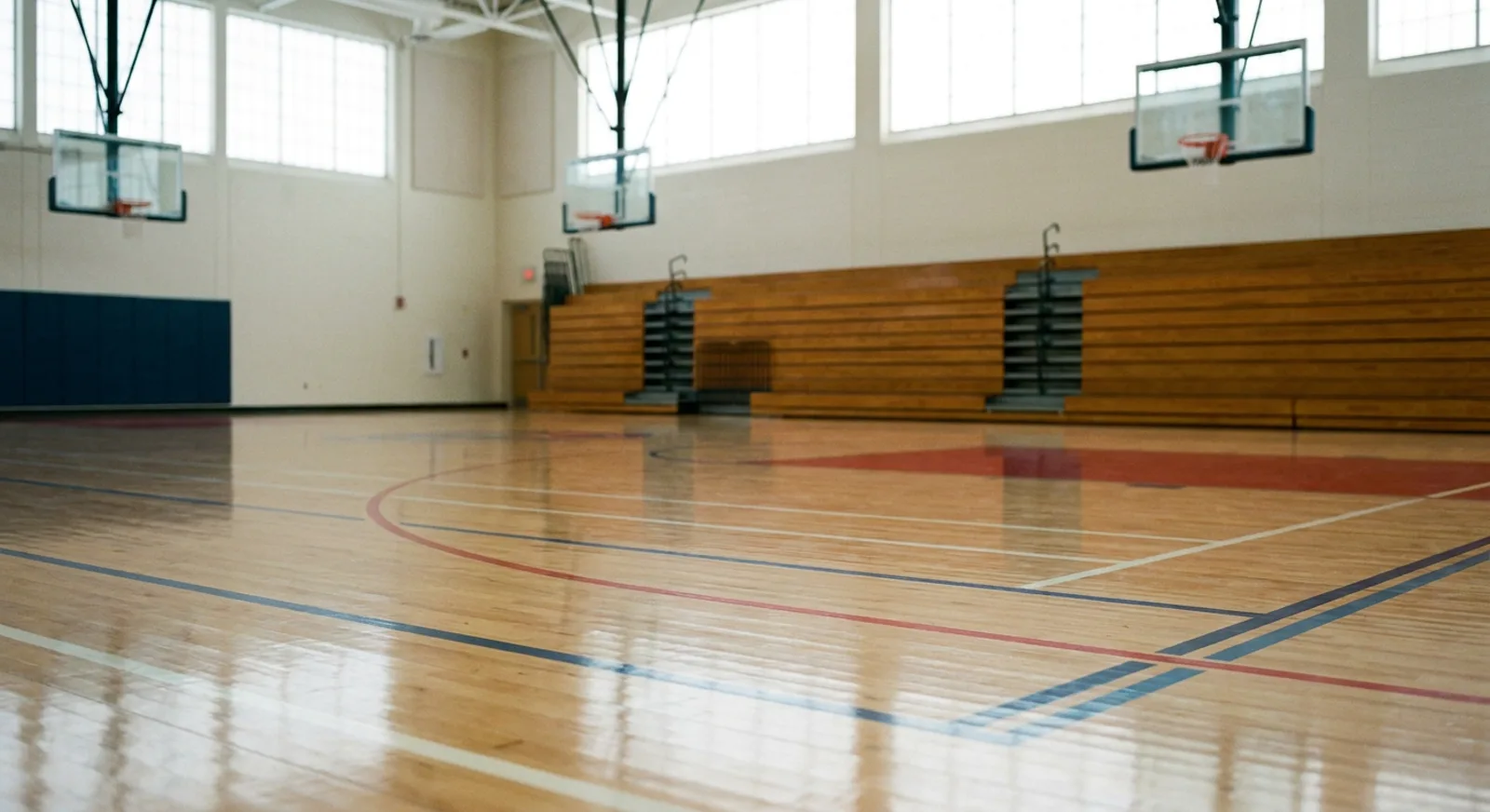Sanded maple hardwood sports court with freshly applied finish, game lines faintly visible, in a New Jersey school gymnasium