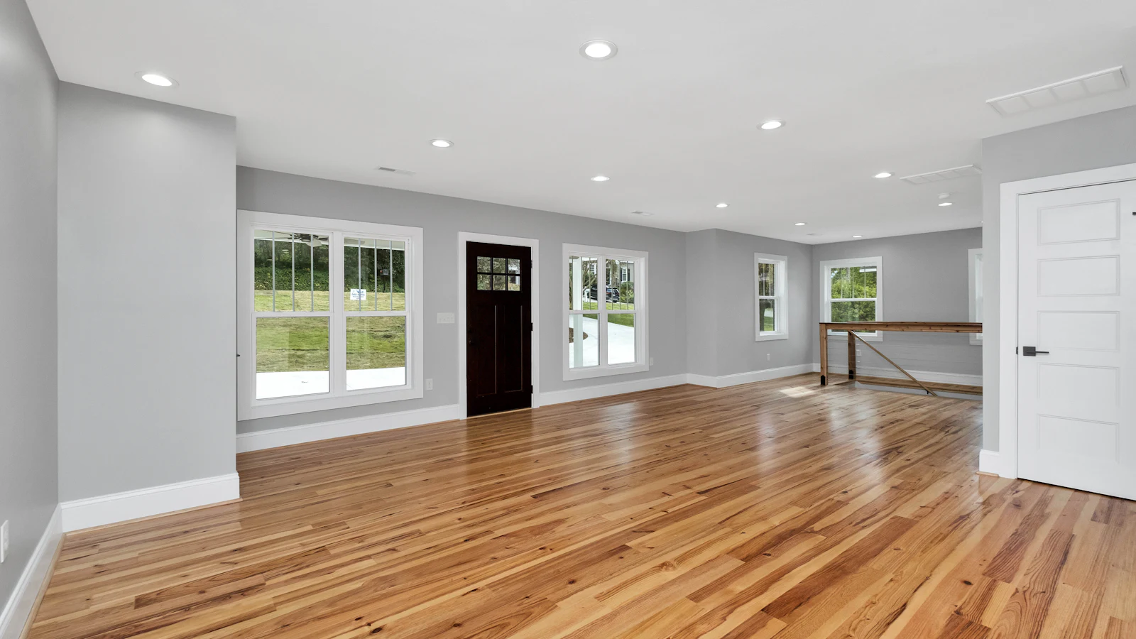 Empty living room with warm, glossy hardwood floors, gray walls, white trim and large windows