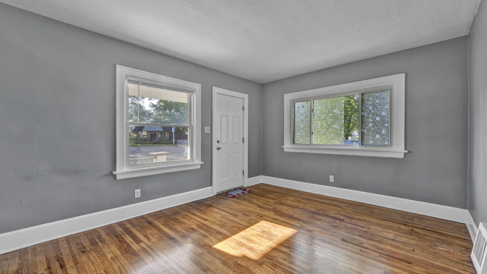 Empty room with gray walls and white trim, a freshly finished hardwood floor and a patch of sunlight