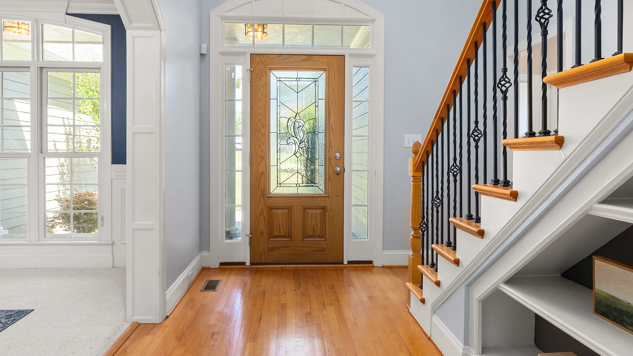 Residential entry hall with oak stair treads, white risers and a wood handrail with iron balusters